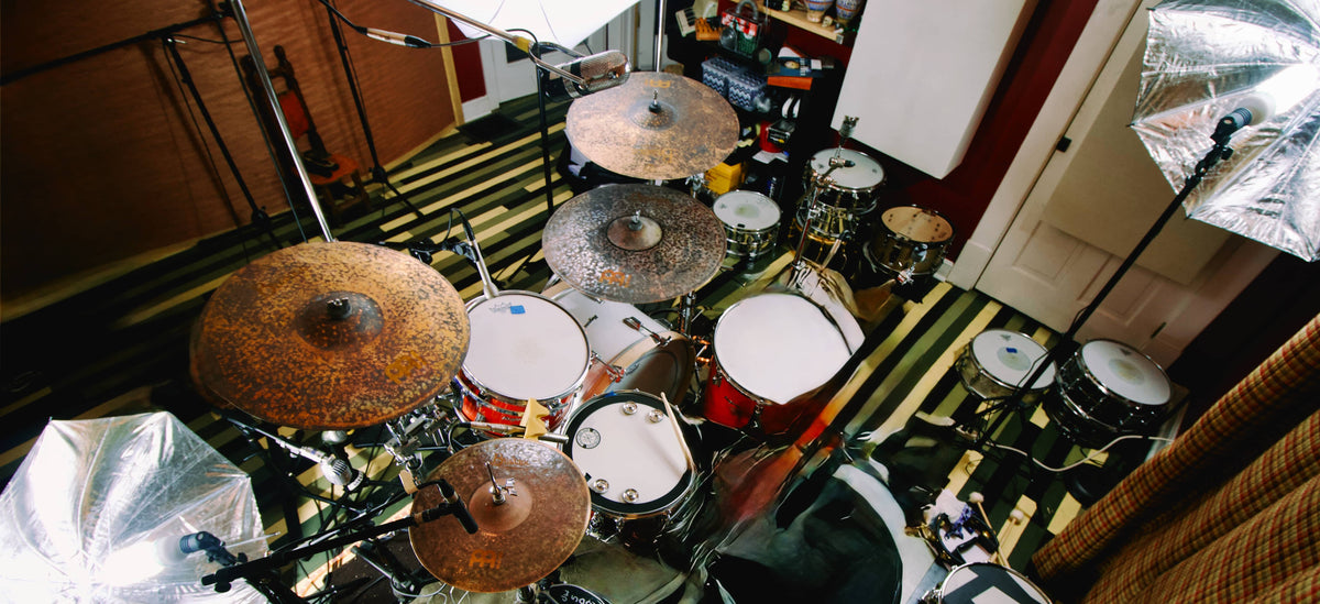 A full drum kit with cymbals, including a prominent Zildjian ride cymbal, set up in a room with studio softbox lights and a striped floor.